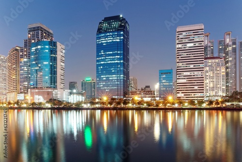 Night skyline of modern skyscrapers by lakeside, with glass curtain walls and dazzling city lights reflected in the smooth lake water in beautiful Benjakiti Park at blue dusk, in Bangkok, Thailand © AaronPlayStation