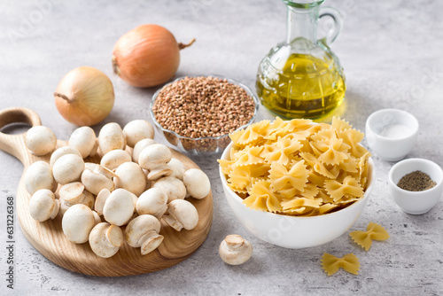 Ingredients: pasta farfalle, buckwheat, fresh champignon mushrooms, onions, olive oil, salt and pepper on a gray textured background. Cooking delicious Jewish dish Kasha varnishkes photo
