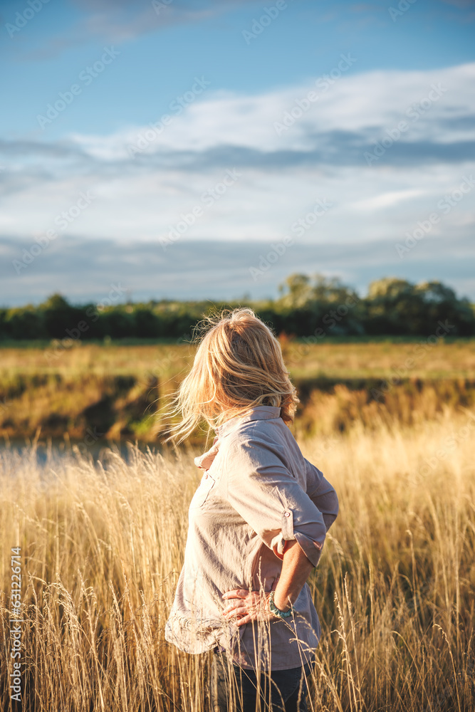 Woman standing in grass at windy lake and feeling connection and harmony with nature Woman standing in grass at windy lake and feeling connection and harmony with nature