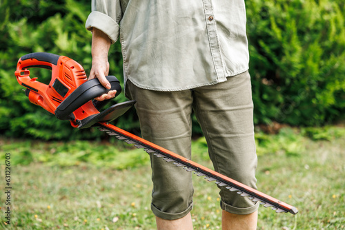 Woman gardener holding electric hedge trimmer. Unrecognizable person is ready for trimming at backyard. Gardening equipment