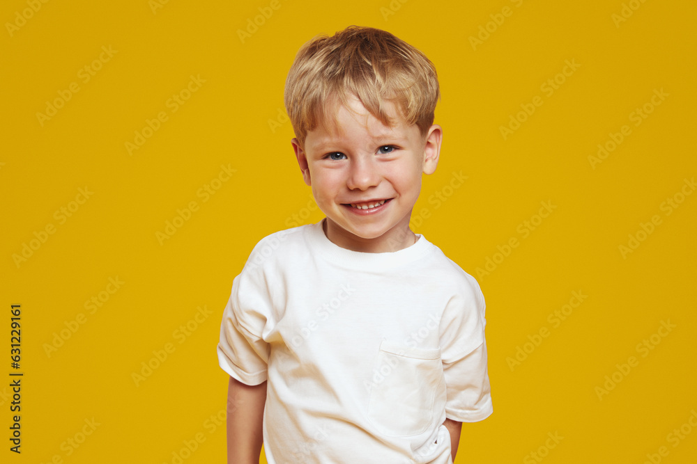 Happy little blonde male kid boy in white tshirt laughing at camera against orange background - obrazy, fototapety, plakaty 
