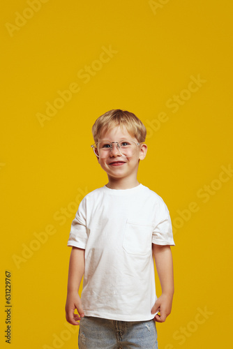 Happy cute pupil boy in stylish white t shirt and eyeglasses smiling and looking excited at camera