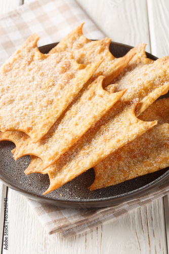 Oreillettes deliciously light and crisp pastry fritters closeup on the plate on the wooden table. Vertical photo