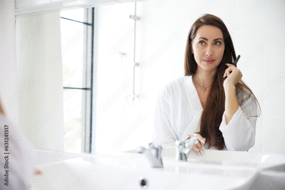 young woman combing hair in front of mirror at bathroom young woman combing hair in front of mirror at bathroom