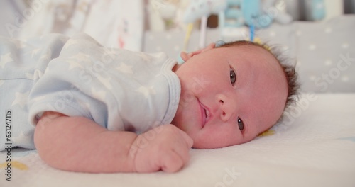 Close up portrait adorable newborn baby infant child girl face wakes up and opens his eyes looking at camera on the bed in the morning at home