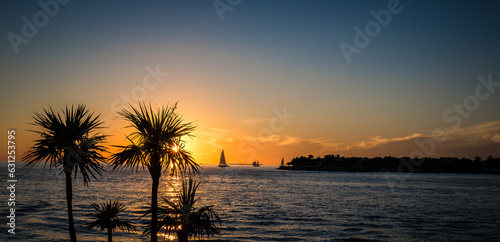 Sun setting of coast of Key West with sailboats, palm trees and clouds