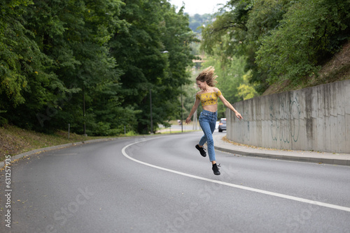 A young beautiful girl is jumping on a bend in the road © Algimantas