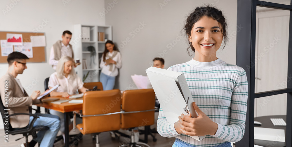 Beautiful young businesswoman with folder in office
