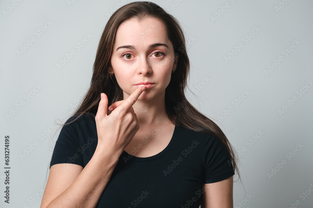 Virus herpes on lips close-up. Beautiful woman holds on finger a cream drop in front of painful lips. Portrait of young beautiful girl European appearance with infection injury. Dermatology sickness Virus herpes on lips close-up. Beautiful woman holds on finger a cream drop in front of painful lips. Portrait of young beautiful girl European appearance with infection injury. Dermatology sickness