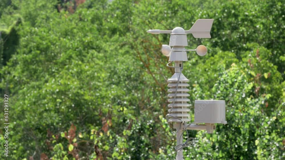 Weather vane and wind sensor of a weather station moving by the action of the air on a sunny and windy day and a blanket of out-of-focus tree leaves in the background Weather vane and wind sensor of a weather station moving by the action of the air on a sunny and windy day and a blanket of out-of-focus tree leaves in the background