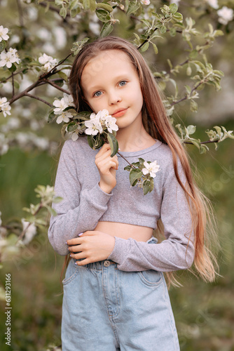 Smiling child girl 6-7 years old in an apple orchard sniffing white flowers of apple trees