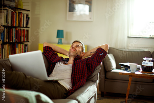 Middle aged man lying down on a couch and using a laptop photo