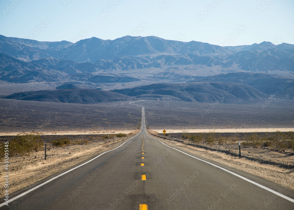 Naklejka premium a desert road leads to the mountains of Death Valley National Park, California, USA