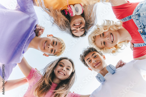 Portrait of smiling multiracial friends wearing colorful t shirts hugging, looking at camera on street. Happy school boys and girls standing together in circle . Vacation, summer, friendship