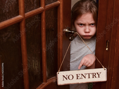 An angry child closes the door to his room and points to a sign that says No entry. The child does not let her parents into the room. Upbringing problems, the conquest of personal space by children