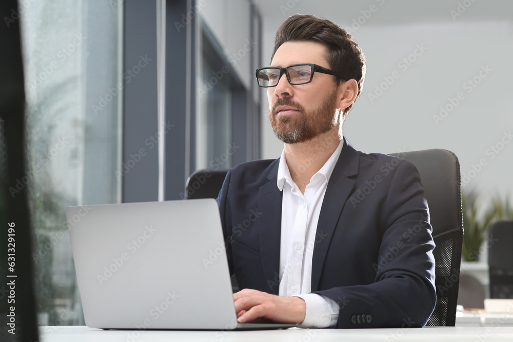 Man working on laptop at white desk in office Man working on laptop at white desk in office