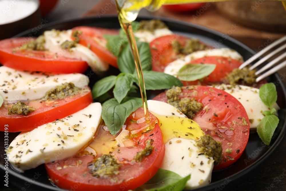 Pouring olive oil onto delicious Caprese salad with pesto sauce on table, closeup Pouring olive oil onto delicious Caprese salad with pesto sauce on table, closeup