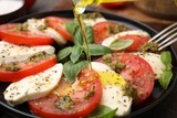 Pouring olive oil onto delicious Caprese salad with pesto sauce on table, closeup