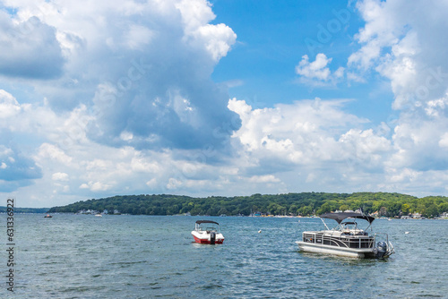 A pontoon boat and pleasure boat anchored in a large lake with white cumulus clouds and a blue sky. photo