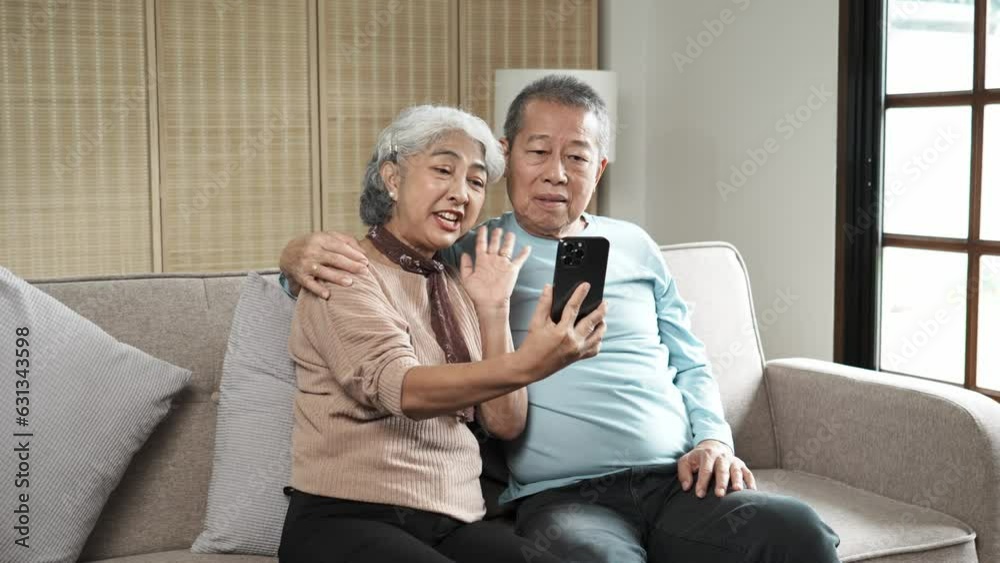 Middle-aged Aaian couple using smartphone together or making video call while sitting at sofa in cozy living room. Middle-aged Aaian couple using smartphone together or making video call while sitting at sofa in cozy living room.