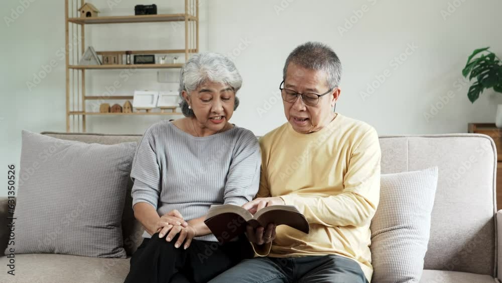 Lovely Asian senior couple reading book together while siting on couch in living room at home. Lovely Asian senior couple reading book together while siting on couch in living room at home.