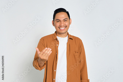 Happy young Asian man wearing casual shirt showing come on gesture with hands isolated on white background