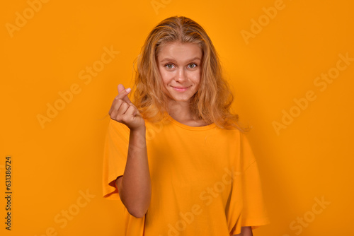 Slika na platnu Young positive beautiful Caucasian woman makes snap of fingers or gesture demanding money to ask for payment for work done and desire to earn stands posing on yellow background