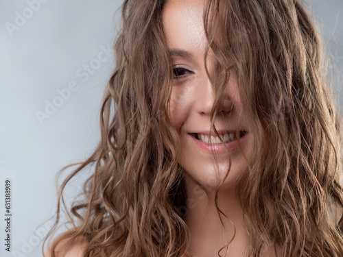 Portrait of a young beautiful woman with wet curls. Close-up on a light background.