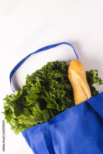 Blue canvas bag with baguette and green salad vegetables and copy space on white background