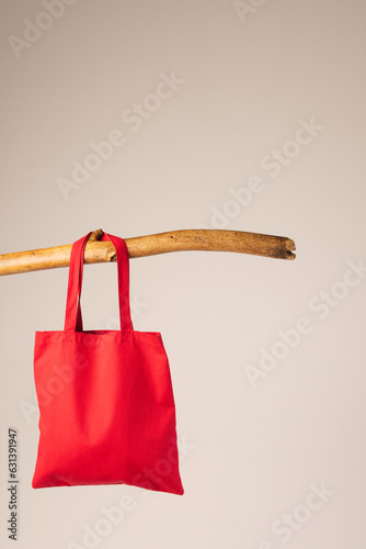 Red canvas bag hanging from wooden branch with copy space on white background