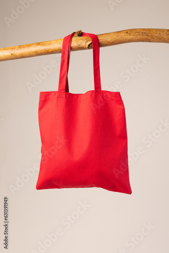 Red canvas bag hanging from wooden branch with copy space on white background
