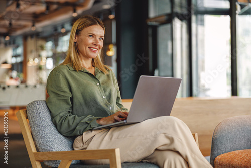 Stylish woman freelancer working on laptop in cozy coworking and looking at side