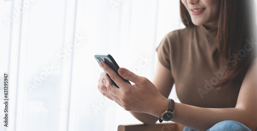 Happy young asian woman checking social media on mobile phone at home. Smiling young woman sitting on sofa using smartphone app for online shopping and mobile banking. people lifestyles