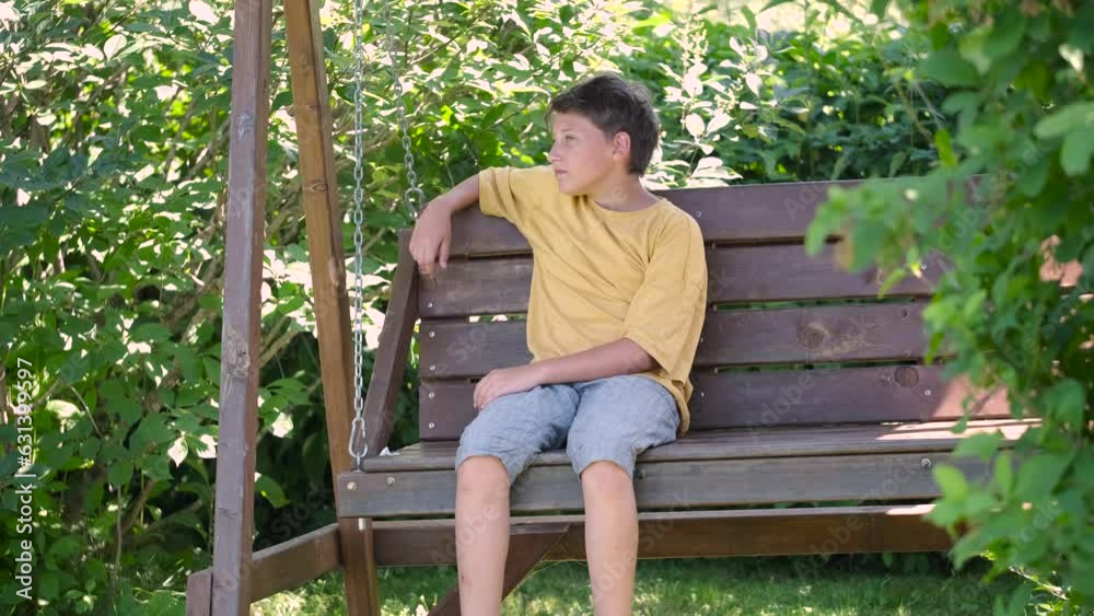 Boy in yellow clothes swinging on swing in a park or kindergarten yard. teen having fun outdoor. Healthy summer activity for children. Boy in yellow clothes swinging on swing in a park or kindergarten yard. teen having fun outdoor. Healthy summer activity for children.