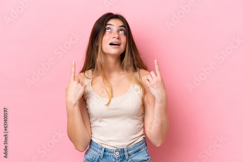 Young caucasian woman isolated on pink background surprised and pointing up