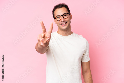 Young caucasian man isolated on pink background smiling and showing victory sign © luismolinero