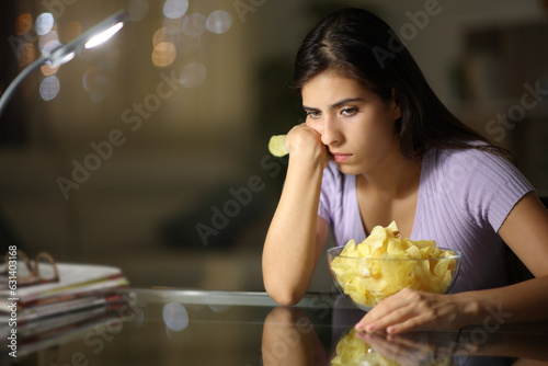 Sad woman eating portato chips complaining in the night photo
