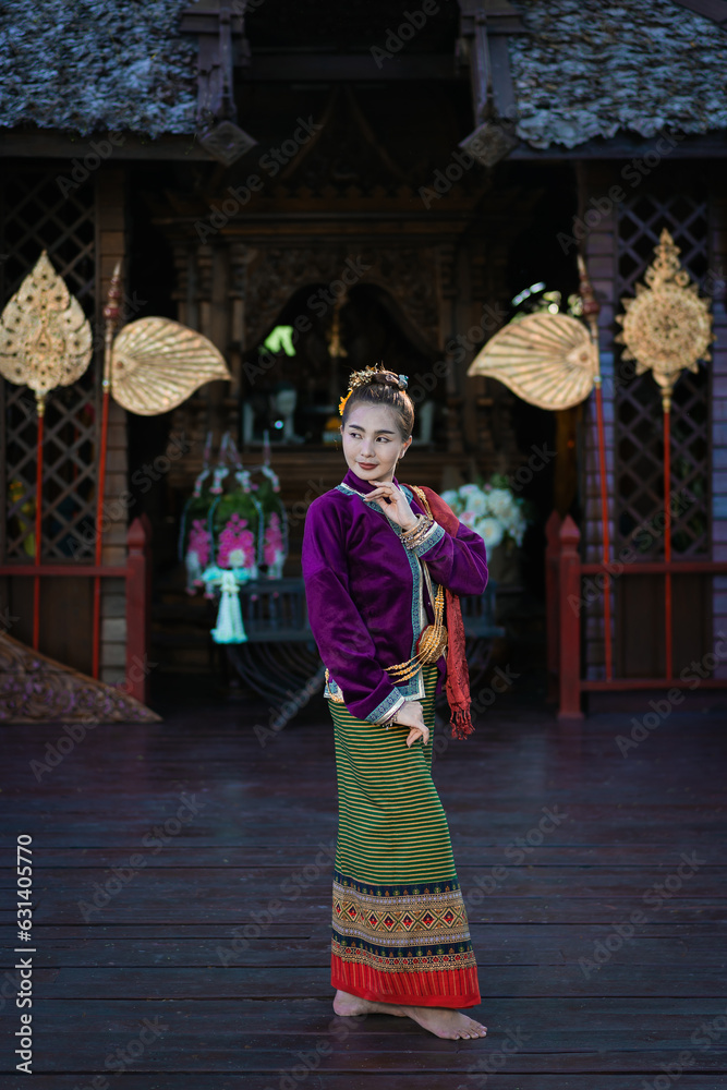 Fototapeta premium Pretty Asian woman wearing ancient native Thai traditional dress costumes standing in the classic Thai house.
