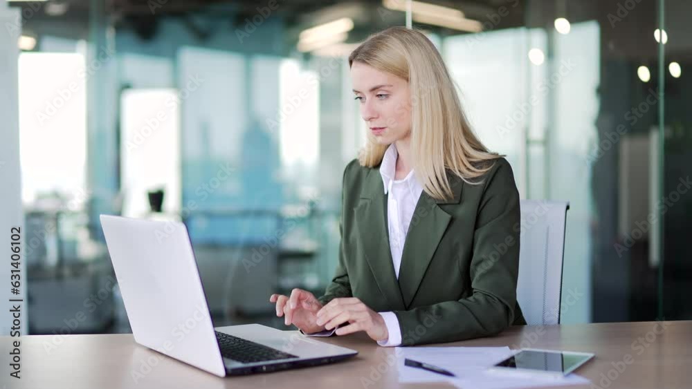 A young confident businesswoman in a suit typing on a laptop while sitting at a workplace in a modern office. Female employee working on a project on the computer, texting a client or chatting online A young confident businesswoman in a suit typing on a laptop while sitting at a workplace in a modern office. Female employee working on a project on the computer, texting a client or chatting online