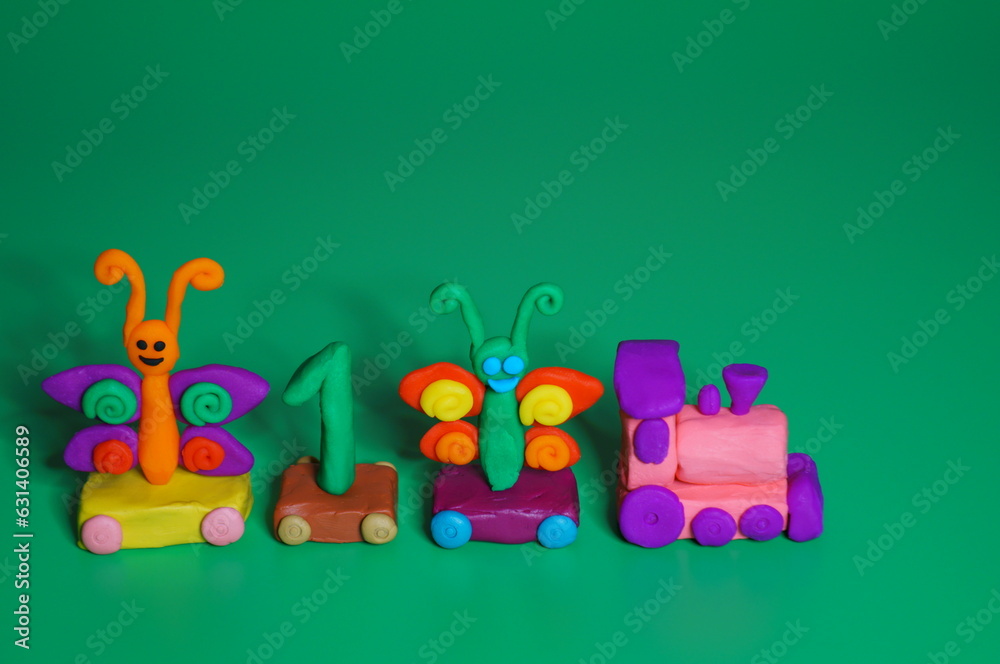Fototapeta premium Toy train made of plasticine with butterflies and the number 1. Birthday. A festive event. Green background.