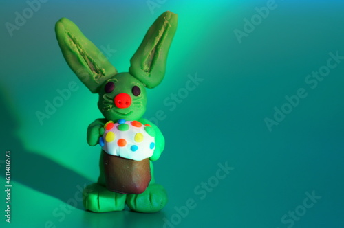 A toy Easter bunny with a cake on a green background.