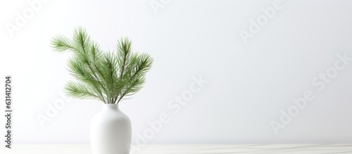 A blank white wall mockup featuring green fir branches in a vase on a white table, perfect for