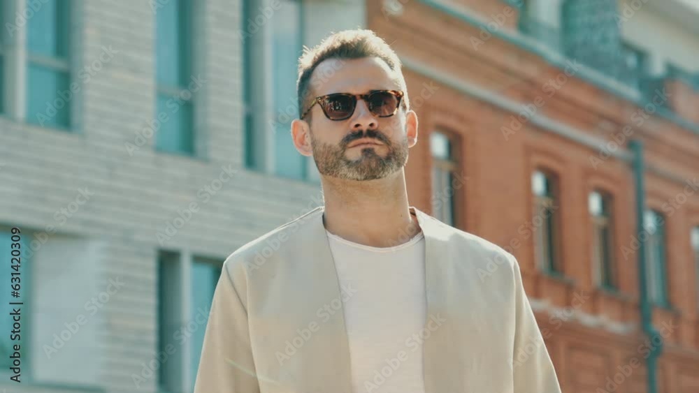 Handsome confident stylish hipster lambersexual model. modern man dressed in elegant white jacket. Fashion male posing in the street background in Europe city at sunset. In sunglasses Handsome confident stylish hipster lambersexual model. modern man dressed in elegant white jacket. Fashion male posing in the street background in Europe city at sunset. In sunglasses