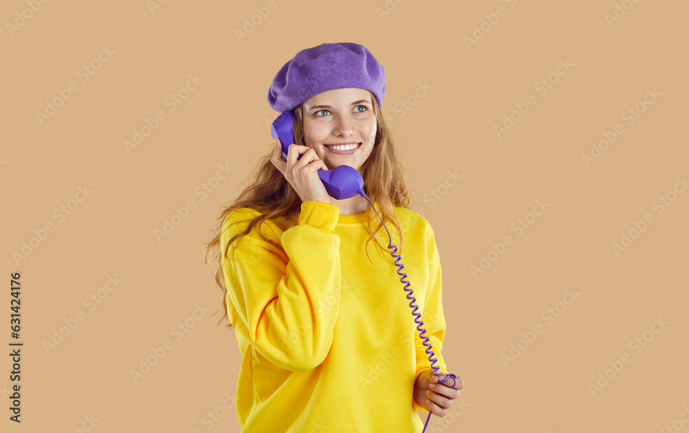 Attractive caucasian girl in grandmothers beret with receiver of old wired telephone near ear. Vintage look in 1980s style. Image in pastel colors isolated on light beige background. Attractive caucasian girl in grandmothers beret with receiver of old wired telephone near ear. Vintage look in 1980s style. Image in pastel colors isolated on light beige background.