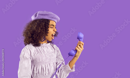 Kid gets angry while talking on phone. Side view studio portrait of annoyed irritated furious curly African child girl in pretty beret hat shouting at landline telephone receiver she's holding in hand