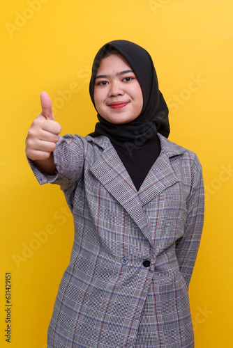 Beautiful young Asian muslim woman with hands thumbs up, showing ok sign isolated on yellow background photo