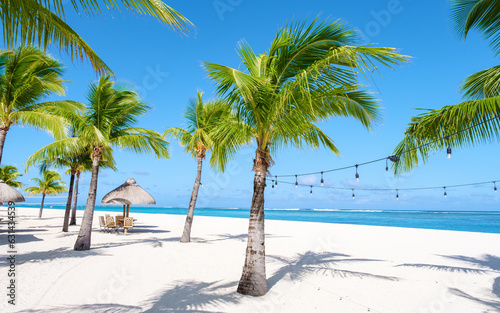 Le Morne beach Mauritius Tropical beach with palm trees, white sand blue ocean and beach beds with umbrellas, sun chairs,, parasols under a palm tree at Mauritius Le Morne with blue sky