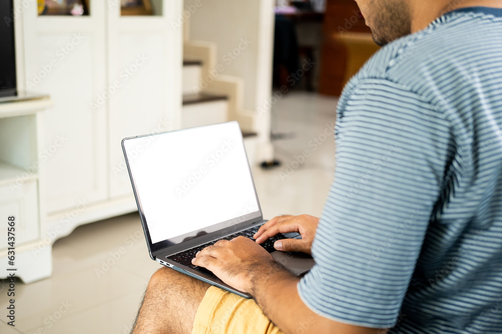 Young man using laptop computer sitting on blue sofa in the house. Man with typing keyboard working with laptop while sitting on couch work from home Young man using laptop computer sitting on blue sofa in the house. Man with typing keyboard working with laptop while sitting on couch work from home