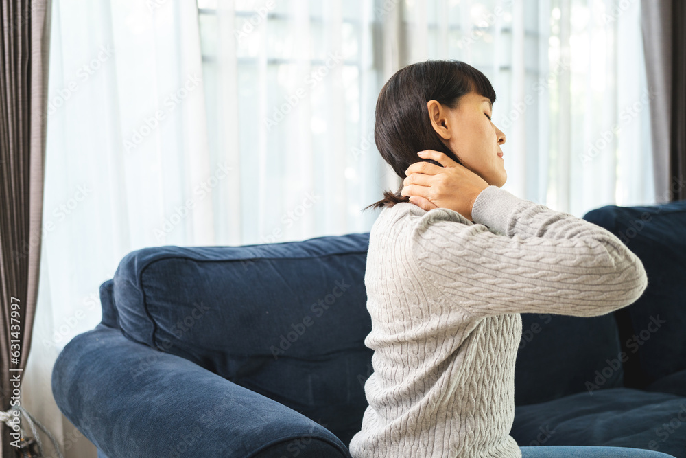 Young woman has problem with structural posture back neck and shoulder pain. Massaged her neck and shoulders for relief. reduce muscle tension on sofa couch in living room Young woman has problem with structural posture back neck and shoulder pain. Massaged her neck and shoulders for relief. reduce muscle tension on sofa couch in living room