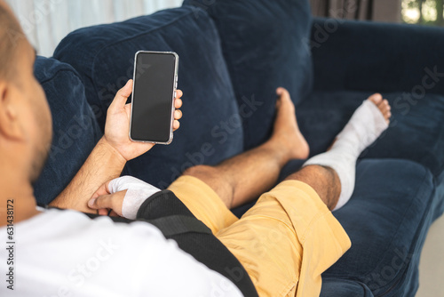 Social security and health insurance concept. Young Man suffer pain from accident fracture broken bone injury with arms splints in cast sling support arm using smartphone in living room. photo